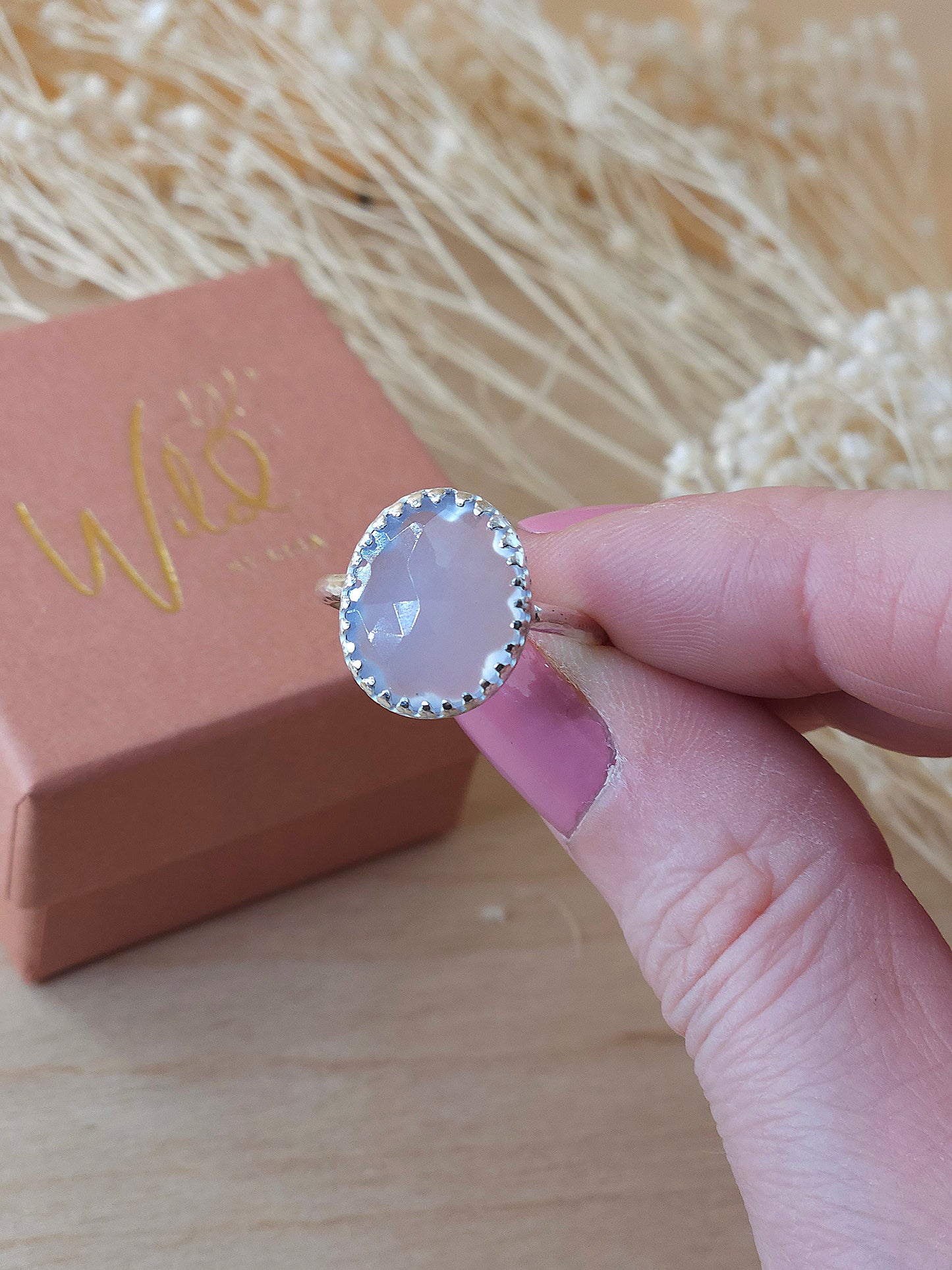 A hand holding a silver ring with chalcedony gemstone. A hidden flower detail can be seen through the translucent gemstone.