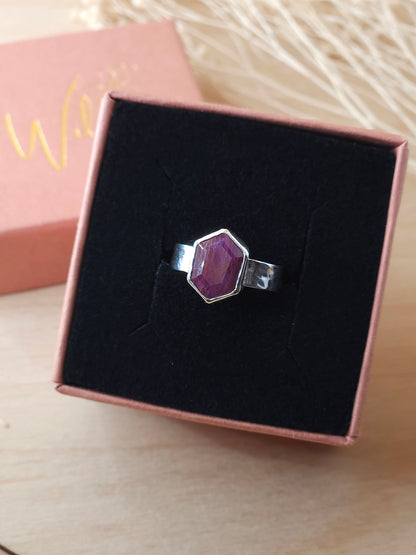 A hexagonal ruby pinkie ring with a lightly hammered band, presented in an open gift box.
