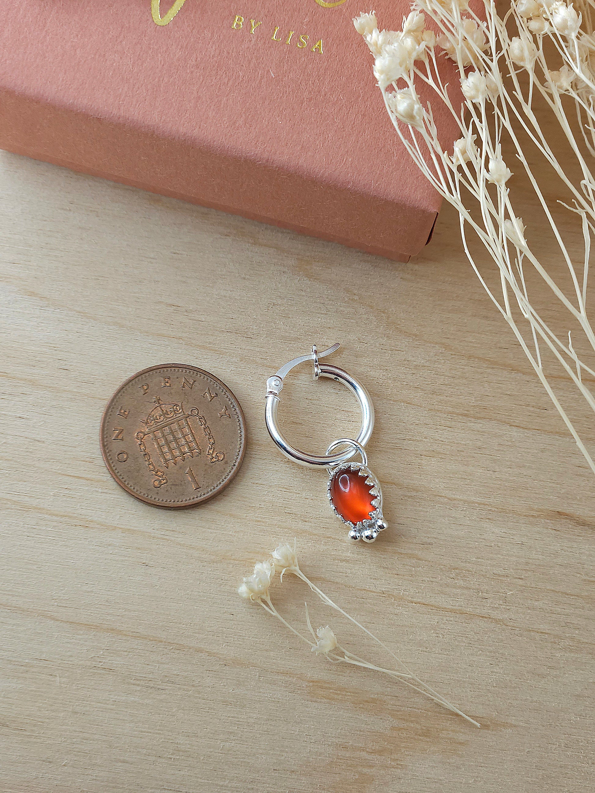 A single silver hoop earring with red carnelian charm lay next to a one pence coin to show the size.