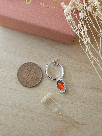 A single silver hoop earring with red carnelian charm lay next to a one pence coin to show the size.