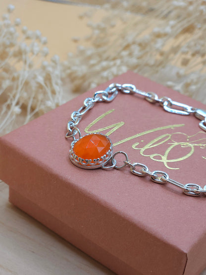 A sterling silver link chain bracelet with orange Carnelian gemstone charm displayed on a terracotta coloured gift box with dried flowers in the background.