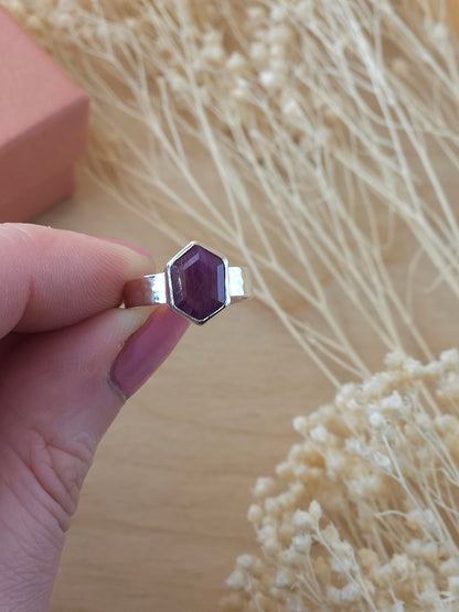 A hand holding a sterling silver hammered pinkie ring with a hexagonal ruby gemstone.