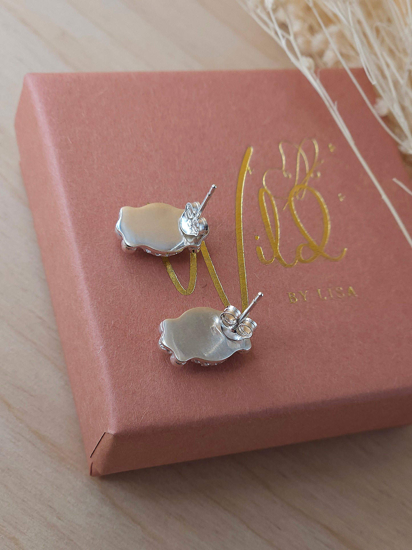 A pair of sterling silver stud earrings displayed on a terracotta coloured gift box showing the back of the earrings including the butterfly backing.