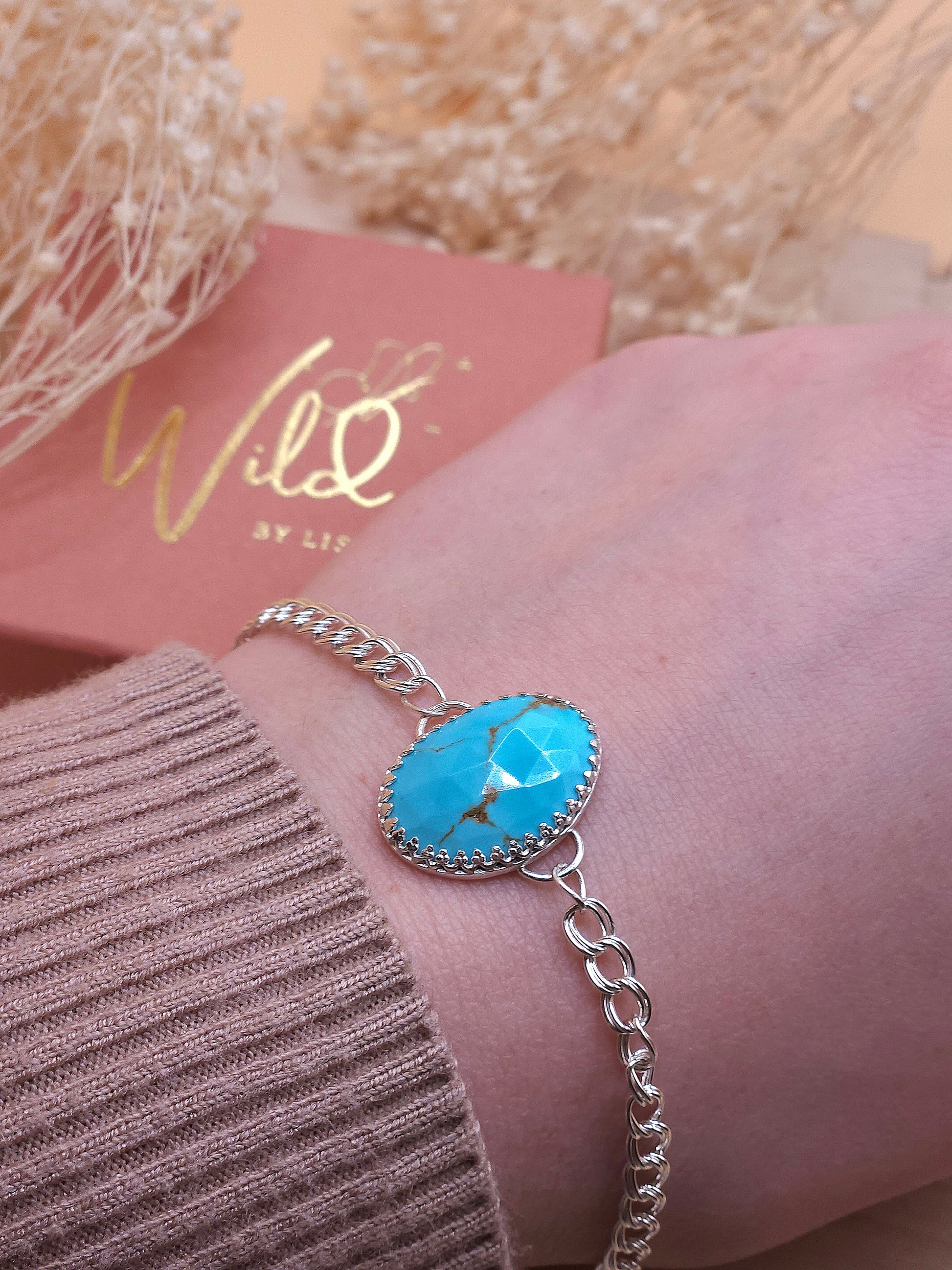 A turquoise silver chain bracelet worn on a wrist, with a gift box and dried flowers in the background.