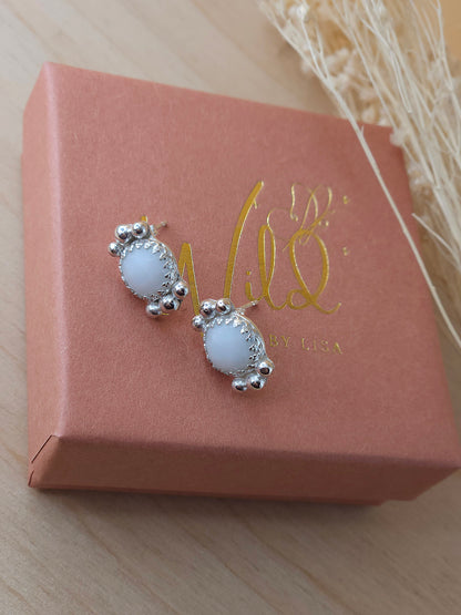 A pair of white agate stud earrings with silver embellishments, presented on a terracotta gift box with gold writing.