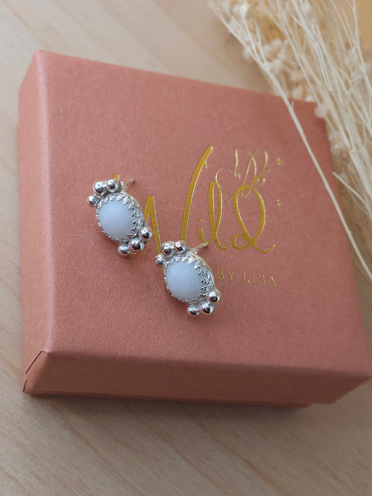 A pair of white agate stud earrings with silver embellishments, presented on a terracotta gift box with gold writing.