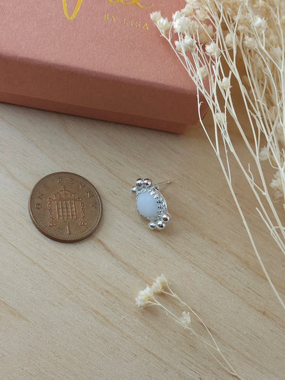 A single white agate silver stud earrings laying next to a one pence coin to show the size comparison. The earring is smaller than the coin.