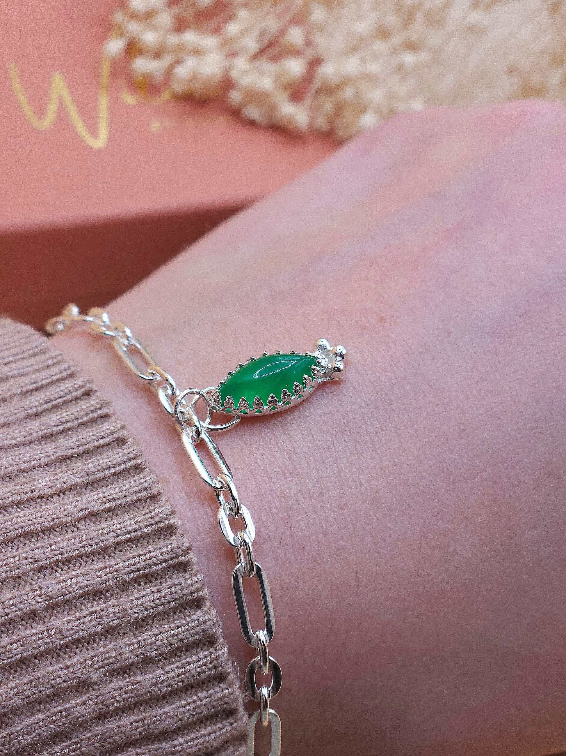 The sterling silver link chain bracelet with green aventurine charm being worn on a wrist. Dried flowers in the background.
