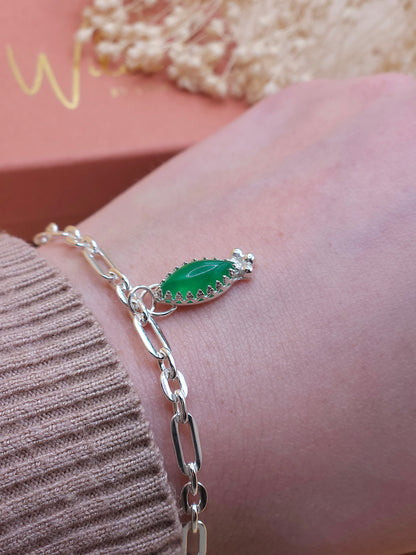The sterling silver link chain bracelet with green aventurine charm being worn on a wrist. Dried flowers in the background.