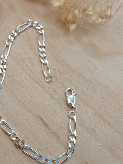 A sterling silver chain bracelet displayed on a wooden background with dried flowers. Showing the lobster clasp.
