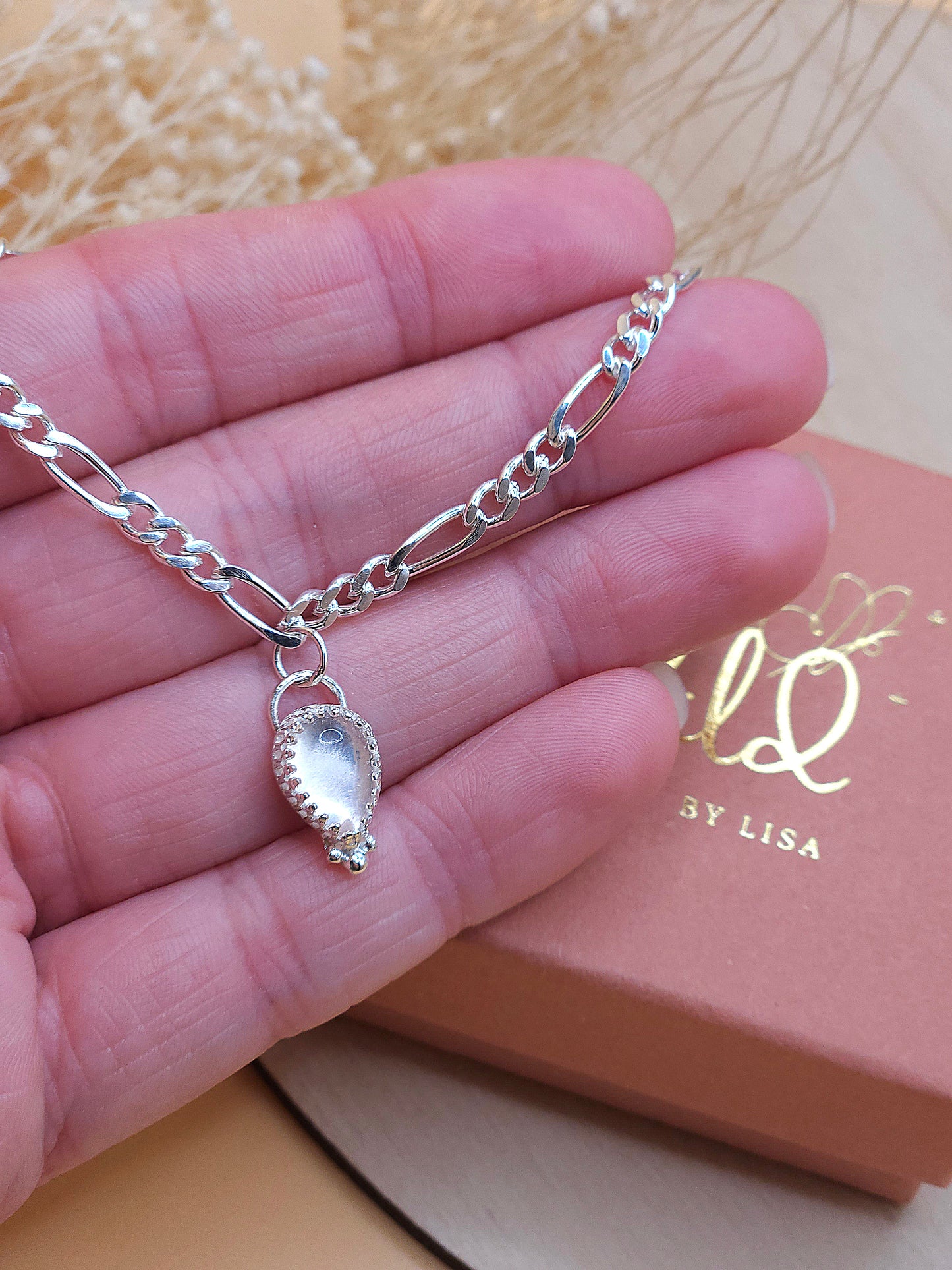 A hand holding the silver chain bracelet with rose quartz gemstone charm.