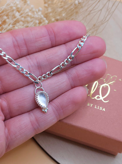A hand holding the silver chain bracelet with rose quartz gemstone charm.