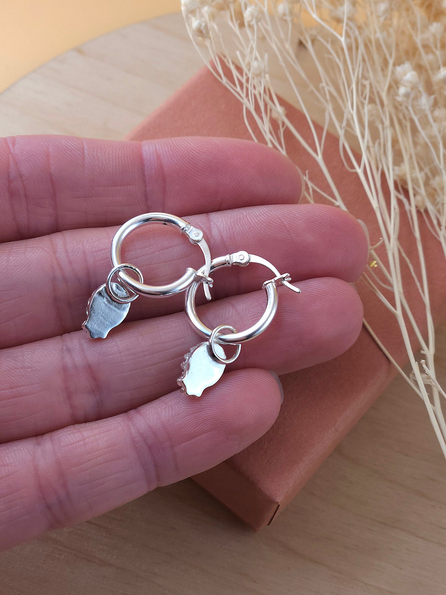 A hand holding a pair of mini silver hoop earrings showing the back of the gemstone setting.