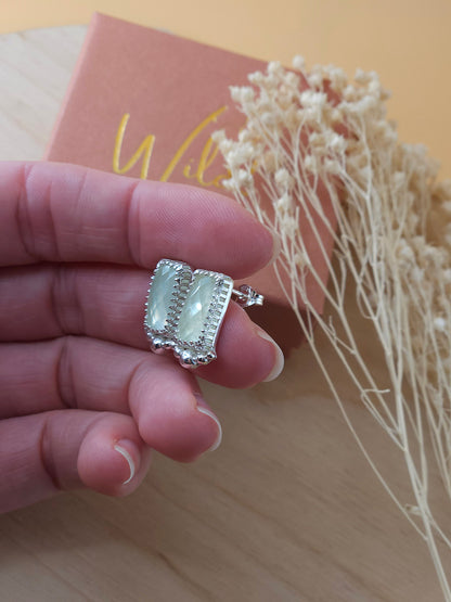 A hand holding a pair of sterling silver stud earrings with green prehnite gemstones and silver embellishments. Showing the side view of the earrings.