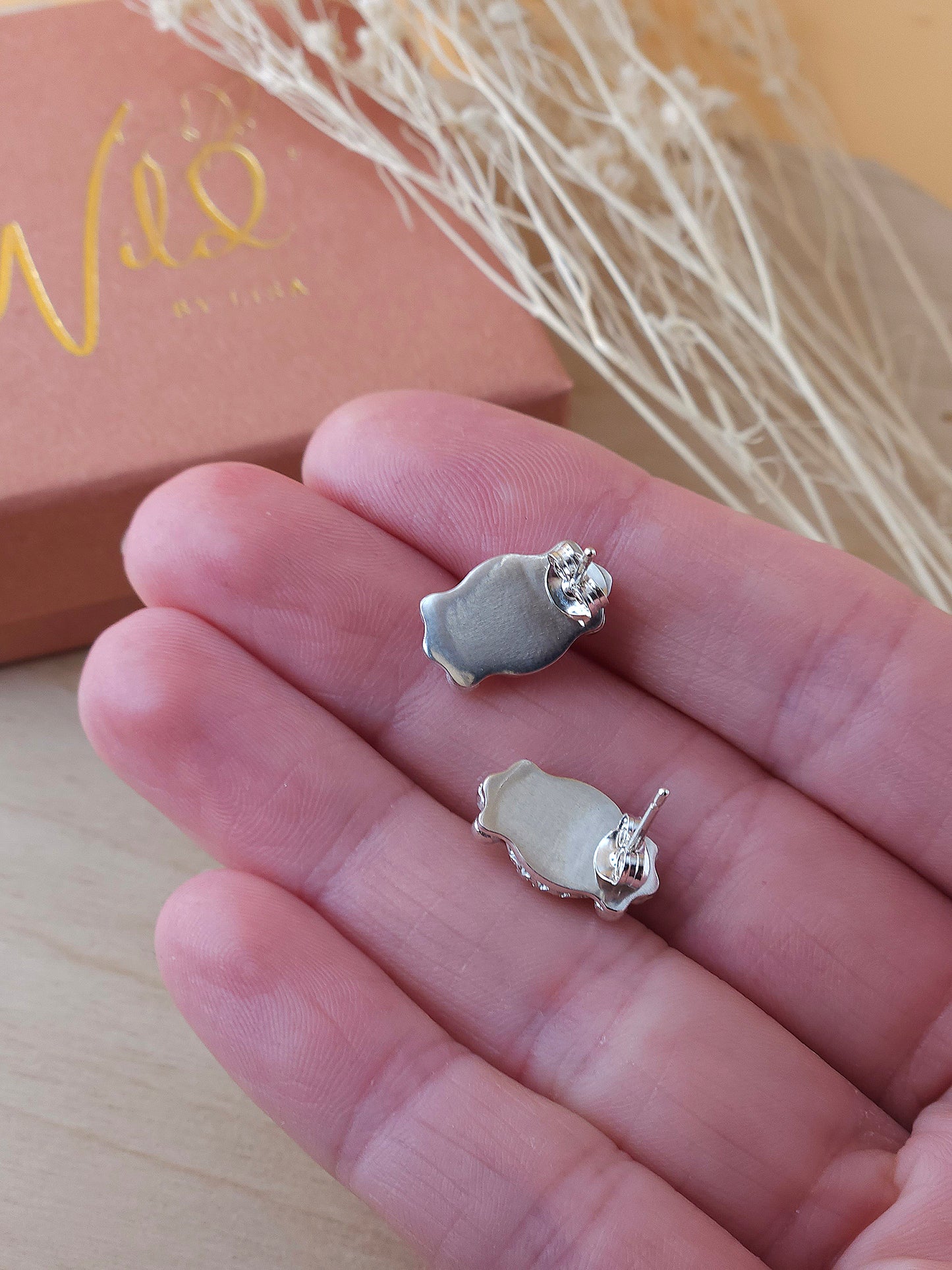 A hand holding a pair of sterling silver gemstone stud earrings show the back view including the butterfly backings.